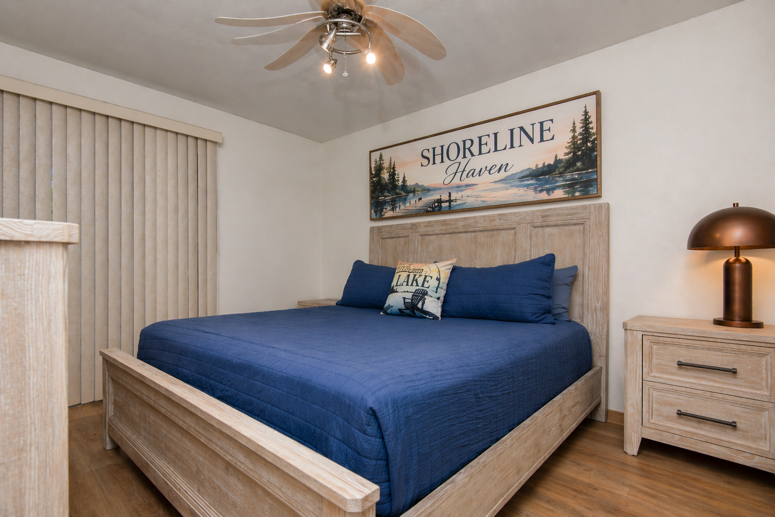 Bedroom with blue bedspread, wood bedframe, and Shoreline Haven wall art